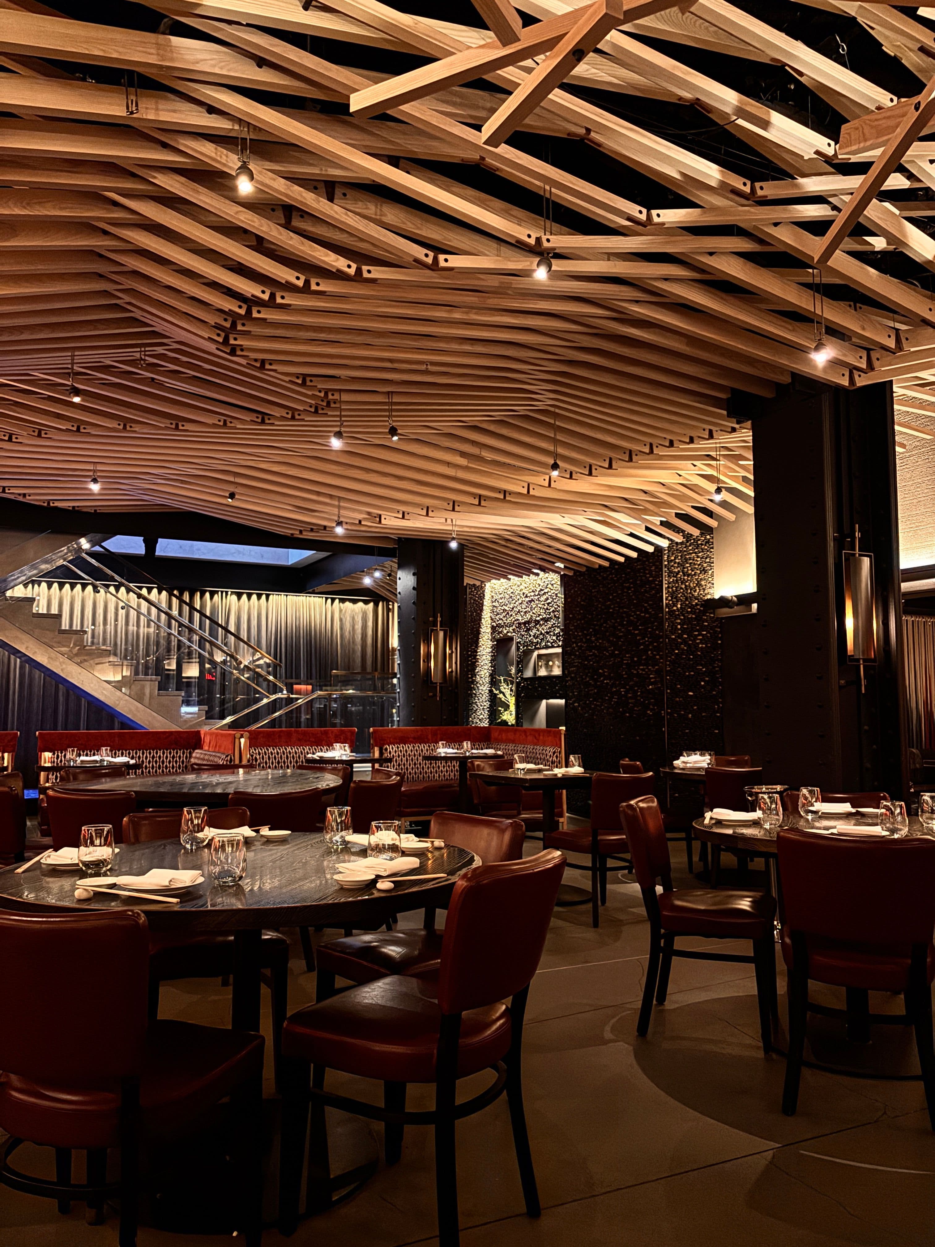 An upscale restaurant dining room with a sculptural wood-beam ceiling